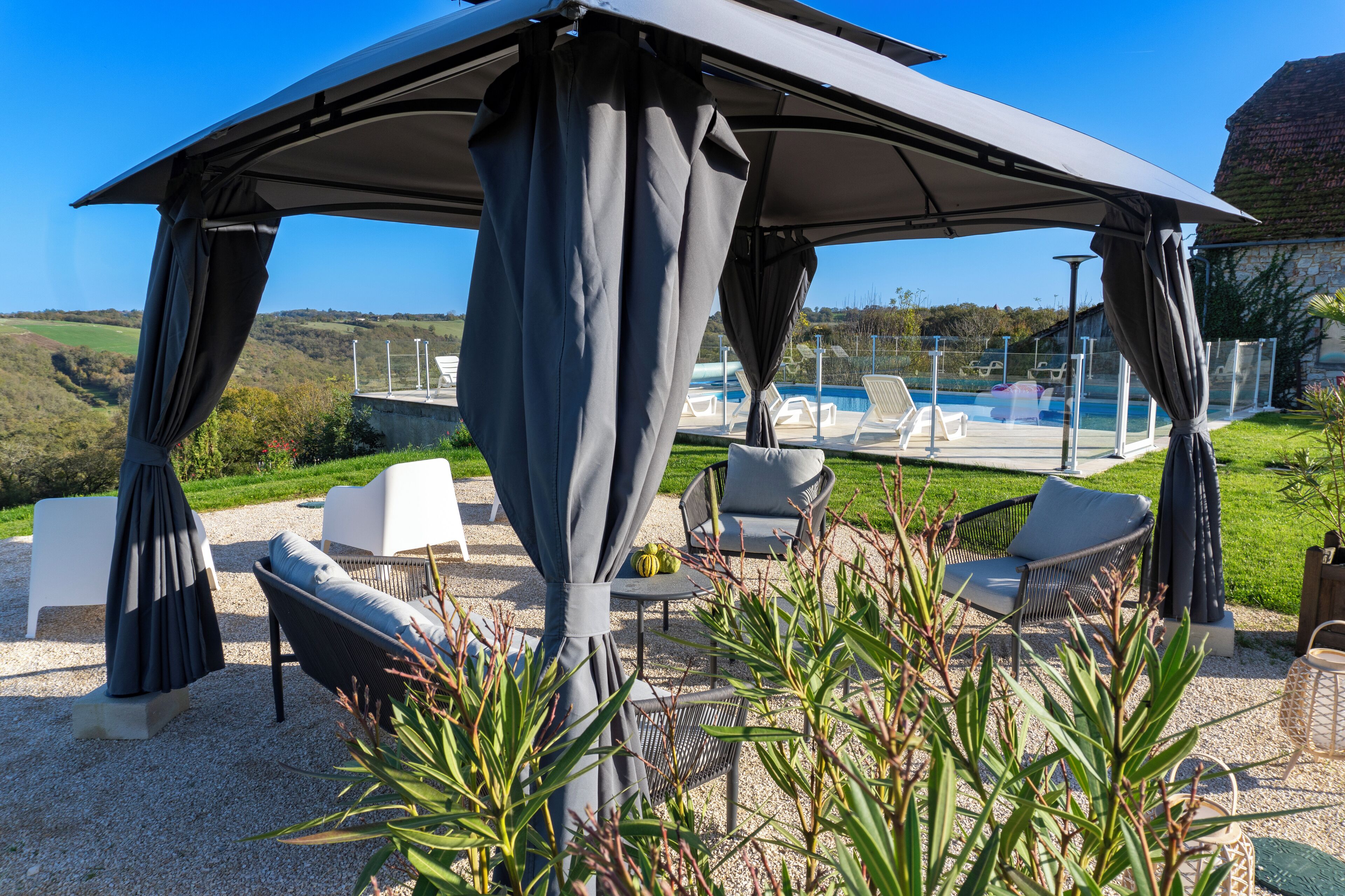 A covered outdoor seating area with a pool in the background.