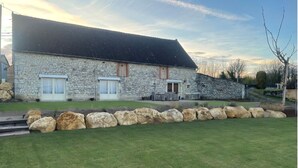 Un bâtiment en pierre avec un toit en pente, deux fenêtres avec volets et un petit porche.