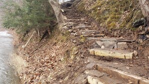 Una escalera de madera que desciende hacia la orilla de un río, rodeada de árboles y paisajes naturales.