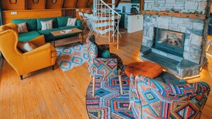 A cozy loft-style room with a wooden ceiling, a stone fireplace, a spiral staircase, and a green sofa. - Boz Bungalov (Sapanca)