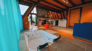 A spacious room with a large bathtub, a stone fireplace, and wooden beams. - Boz Bungalov (Sapanca)