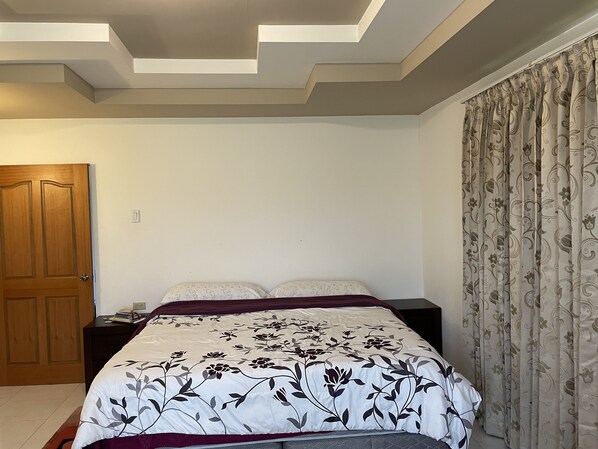Une chambre à coucher avec un lit, des tables de chevet, une porte en bois et un rideau à motifs.