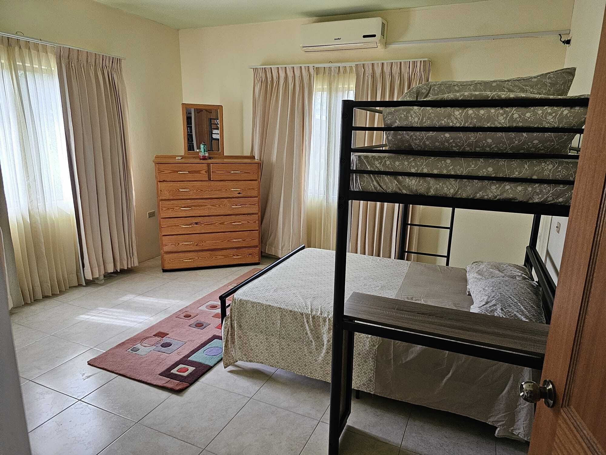 Una habitación con una cama litera, un aparador de madera, un espejo y un tapete estampado.