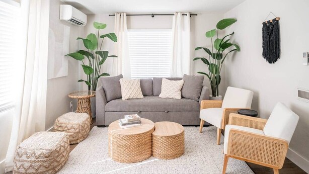 A modern living room with a grey sofa, round wooden coffee tables, and wicker furniture.