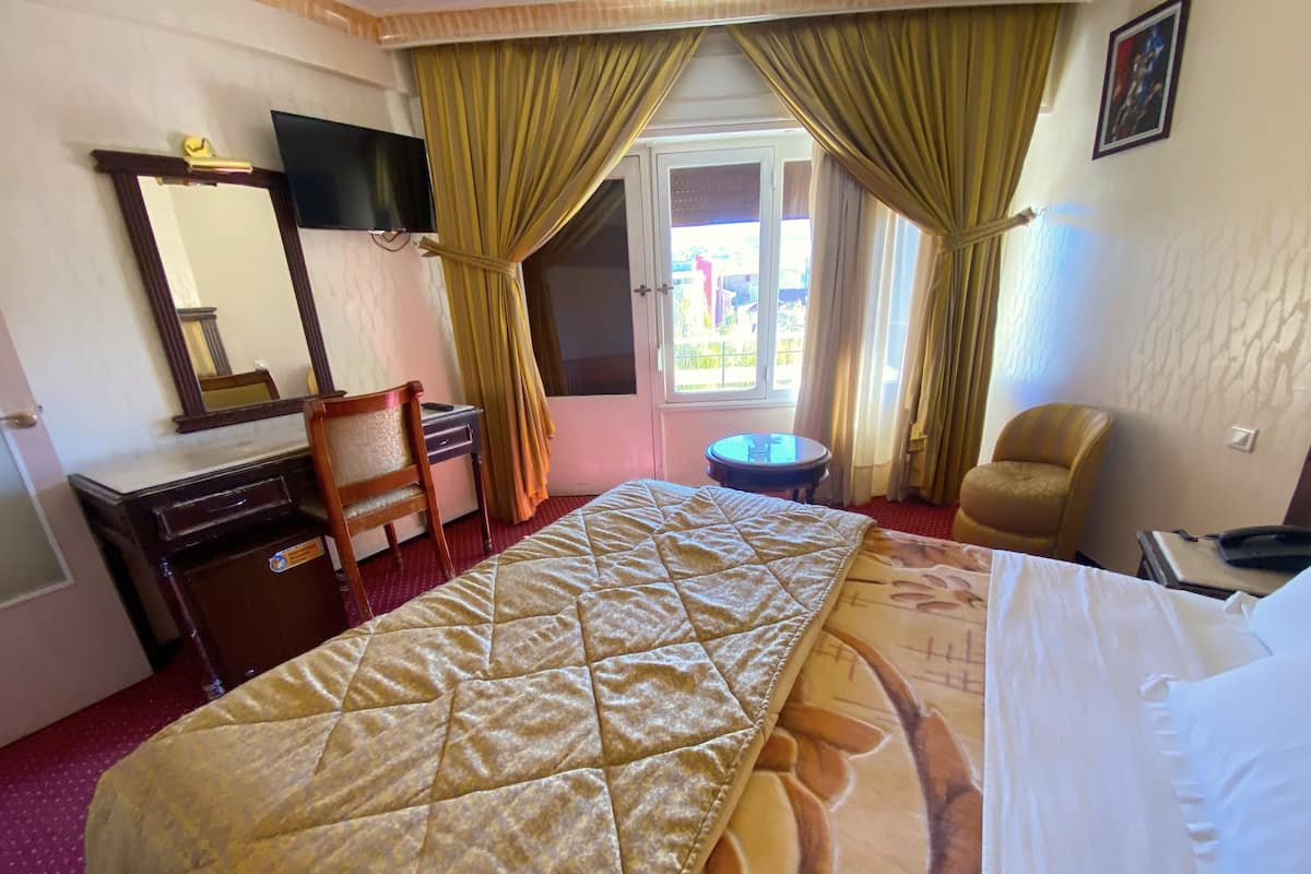 A hotel room with a bed, a desk, a chair, a television, and a window with curtains.