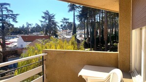 A balcony with a white table and chairs, overlooking a residential area with trees and houses. - Hôtel Tidghine (Issaguen)