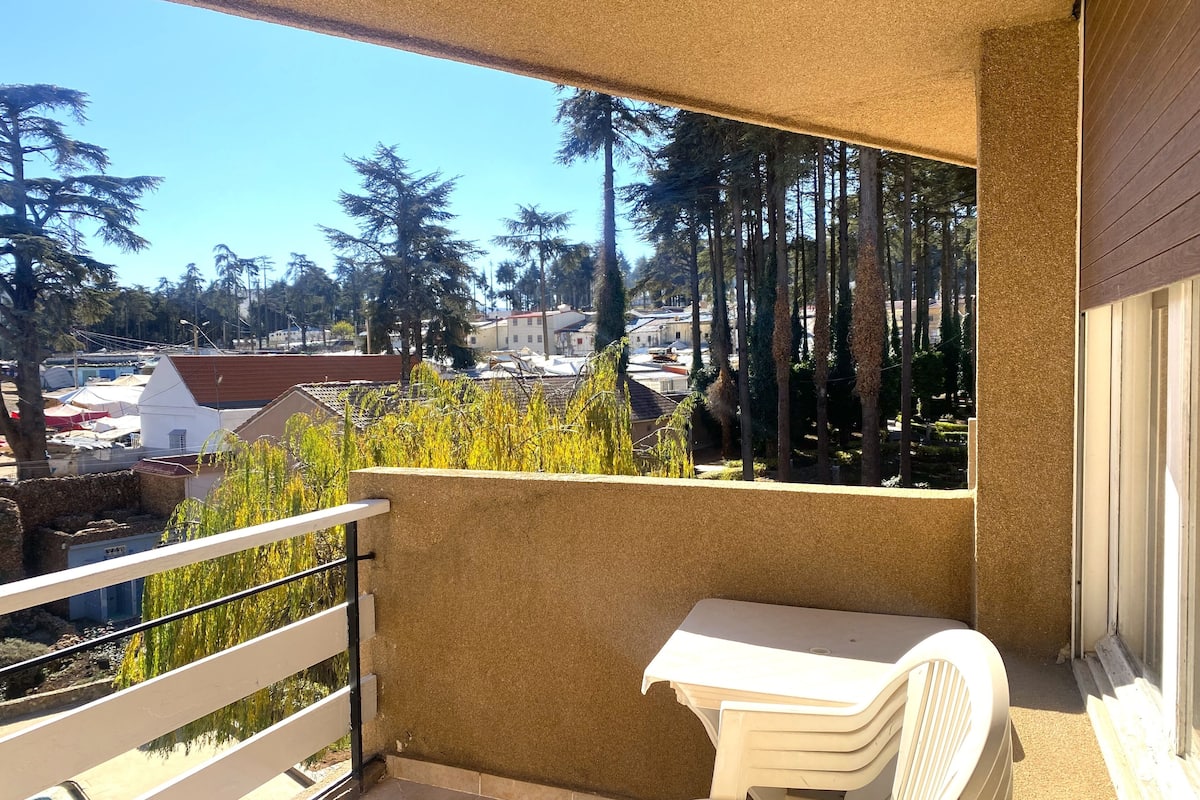 A balcony with a white table and chairs, overlooking a residential area with trees and houses.
