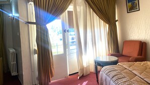 A hotel room with a bed, a chair, a small table, and curtains. - Hôtel Tidghine (Issaguen)