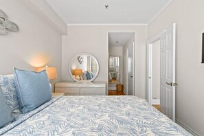 Een slaapkamer met een bed, een ronde spiegel, een dressoir en een deur die naar een andere kamer leidt.