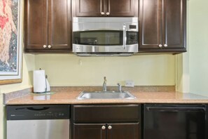 A kitchen with dark wooden cabinets, a stainless steel microwave, a sink with a faucet, and a dishwasher. - Bliss 1br/Pool/StepsToBeach/Dine (Palm Beach)