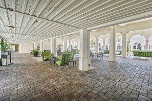 A covered outdoor area with brick flooring, green chairs, and tables, featuring a white ceiling and columns. - Bliss 1br/Pool/StepsToBeach/Dine (Palm Beach)