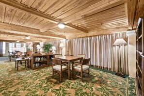 A room with a wooden ceiling, a dining table with chairs, a bookshelf, and a patterned carpet.
