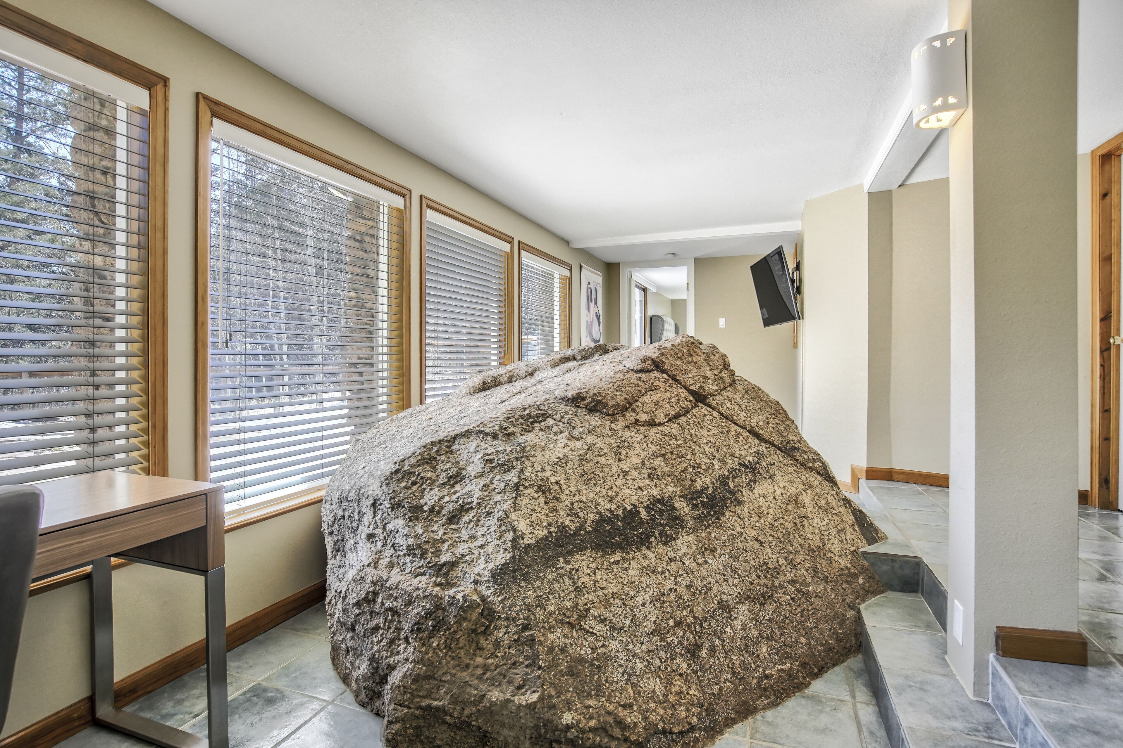 A spacious hallway with large windows, a stone sculpture, and a flat-screen TV mounted on the wall.