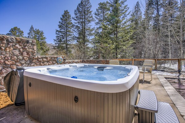 A hot tub with a stone wall backdrop, surrounded by a wooden deck and outdoor furniture. - Stone Statesroom (Cascade)