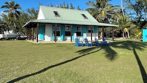 A two-story building with a green roof, a covered porch with blue chairs, and a grassy lawn. - Slice of paradise experience on 3rd largest reef in the world. Fish & Snorkeling (Mangrove Cay)