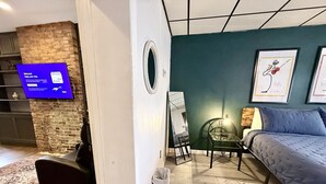A modern room with a bed, a small table, a chair, a mirror, and a TV displaying a welcome message. - Convenient 1 BR close southside (Pittsburgh)