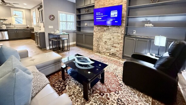 A modern living room with a sofa, coffee table, and a TV mounted on a brick wall. - Convenient 1 BR close southside (Pittsburgh)