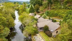 A cabin-style building with a sloped roof, surrounded by dense forest and a river. - Life on the River at the Cabin (Ellijay)