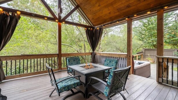 A covered outdoor deck with a table and chairs, surrounded by wooden railings and a view of trees. - Life on the River at the Cabin (Ellijay)