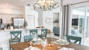A modern kitchen with white cabinets, a stainless steel refrigerator, and a dining area with a wooden table set for four. - Lakefront Naples Lely Resort, 3BR Heated Pool + Players Club & Spa Access Option (Naples)