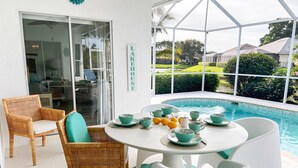 A poolside area with a table set for tea, wicker chairs, and a sign reading "LAKEHOUSE". - Lakefront Naples Lely Resort, 3BR Heated Pool + Players Club & Spa Access Option (Naples)
