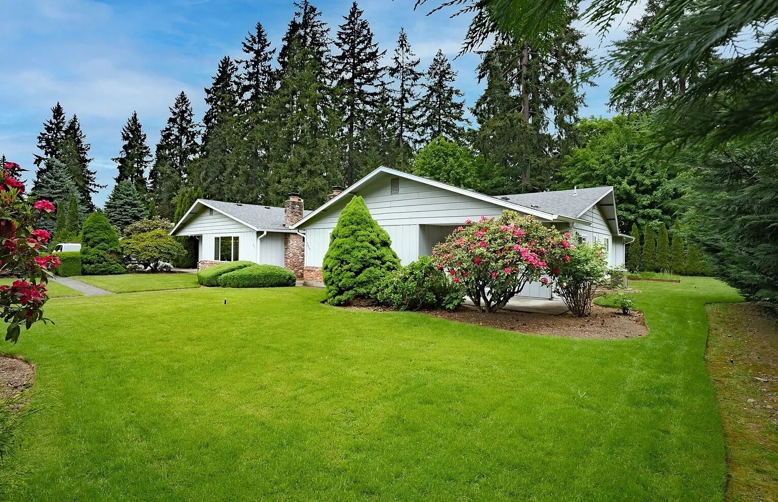 A two-story house with a well-maintained lawn and a variety of shrubs and flowers.