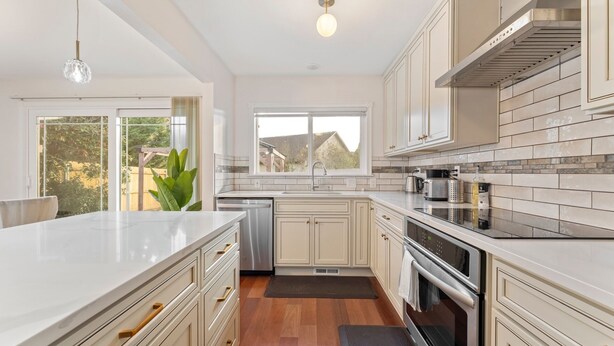 A modern kitchen with white cabinetry, stainless steel appliances, and a large window providing a view of the outdoors.
