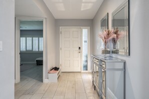 A hallway with a white door, a vanity with a mirror, and a shoe rack.