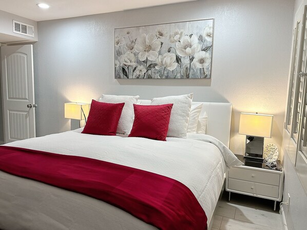 A neatly arranged bedroom with a bed, two bedside tables with lamps, a door, and a wall-mounted artwork. - Scottsdale Charm in Old Town (Scottsdale)