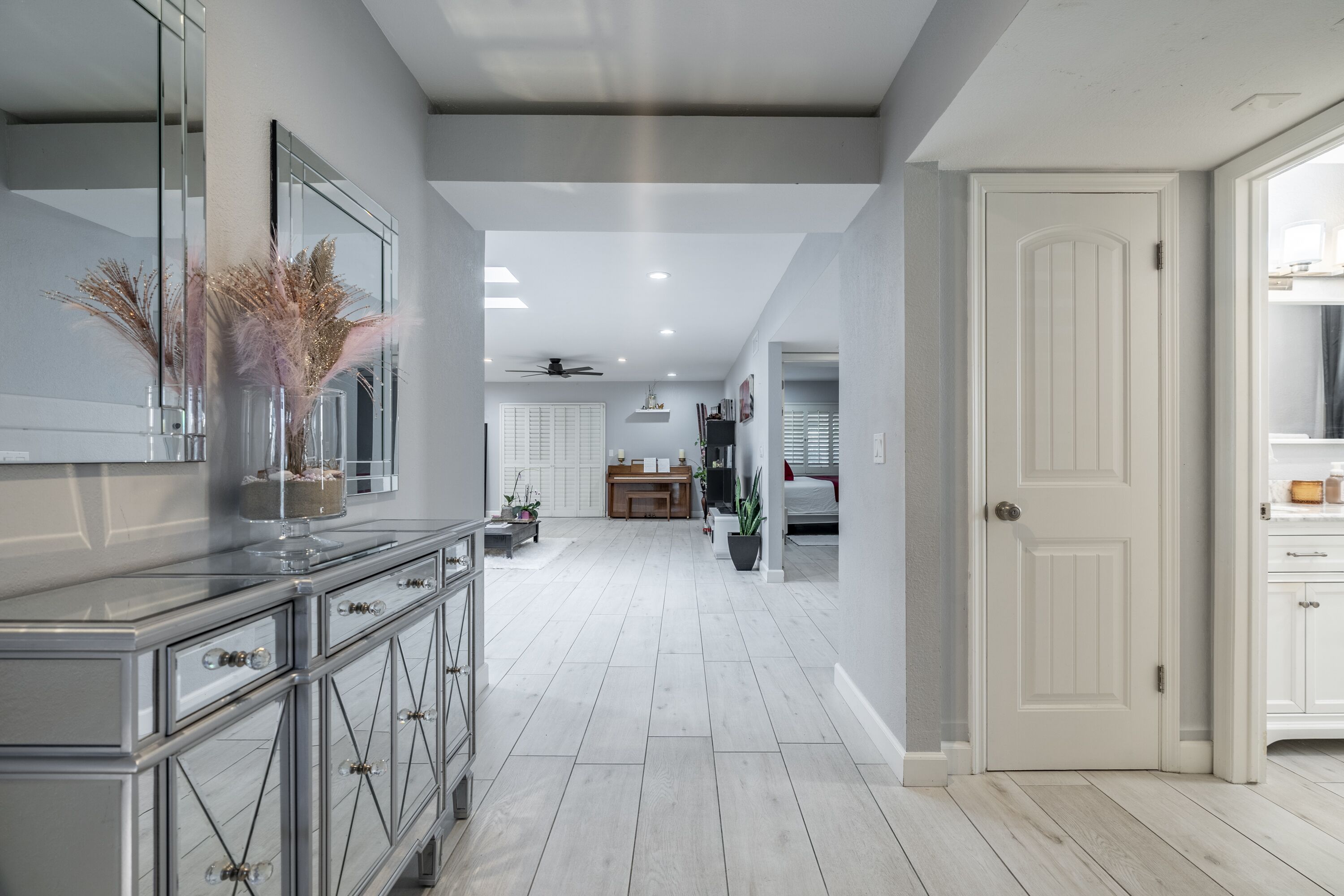 A modern kitchen with a central island, a dining area with a chandelier, and a hallway leading to a bedroom.
