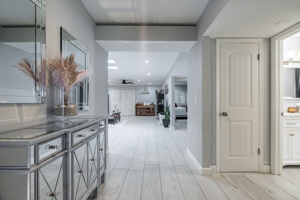 A modern kitchen with a central island, a dining area with a chandelier, and a hallway leading to a bedroom.