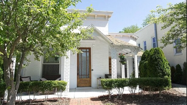 A white house with a wooden door, a covered porch, and a well-maintained garden.