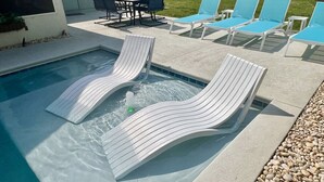 Una piscina con dos sillas de descanso y una mesa con sillas.