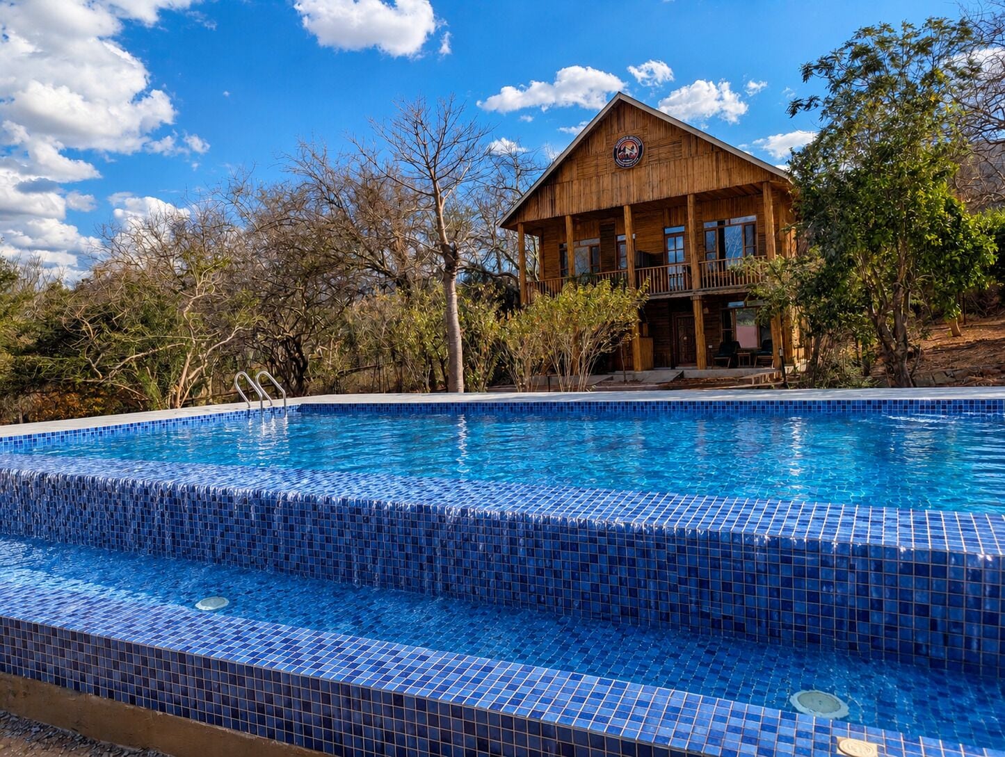 Una piscina con mosaicos azules, rodeada por un edificio de madera con balcones.