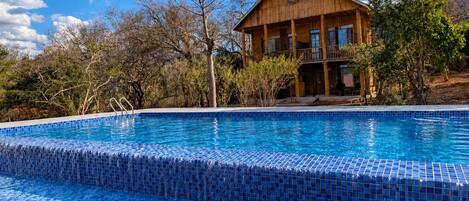 Une piscine aux carreaux de mosaïque bleus, entourée d’un bâtiment en bois doté de balcons.