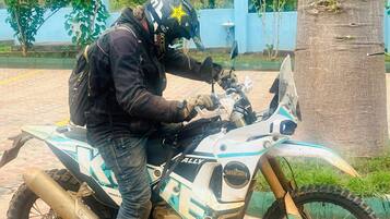 Une personne assise sur une moto, portant un casque et un sac à dos.