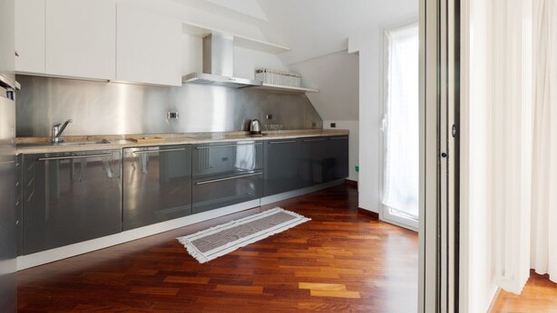 A modern kitchen with stainless steel appliances, grey cabinets, and a wooden floor.
