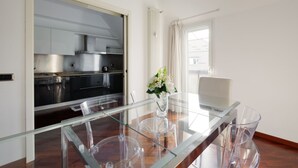 A modern kitchen with stainless steel appliances, a glass dining table with chairs, and a view of the city through a window.