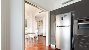 A modern kitchen with stainless steel appliances, a dining area with clear chairs, and a wooden floor.
