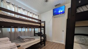 A bunk bed room with a television mounted on the wall, a wooden floor, and a door.
