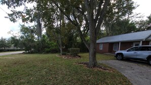 A residential area with a grassy lawn, a tree, a parked car, and a brick building.