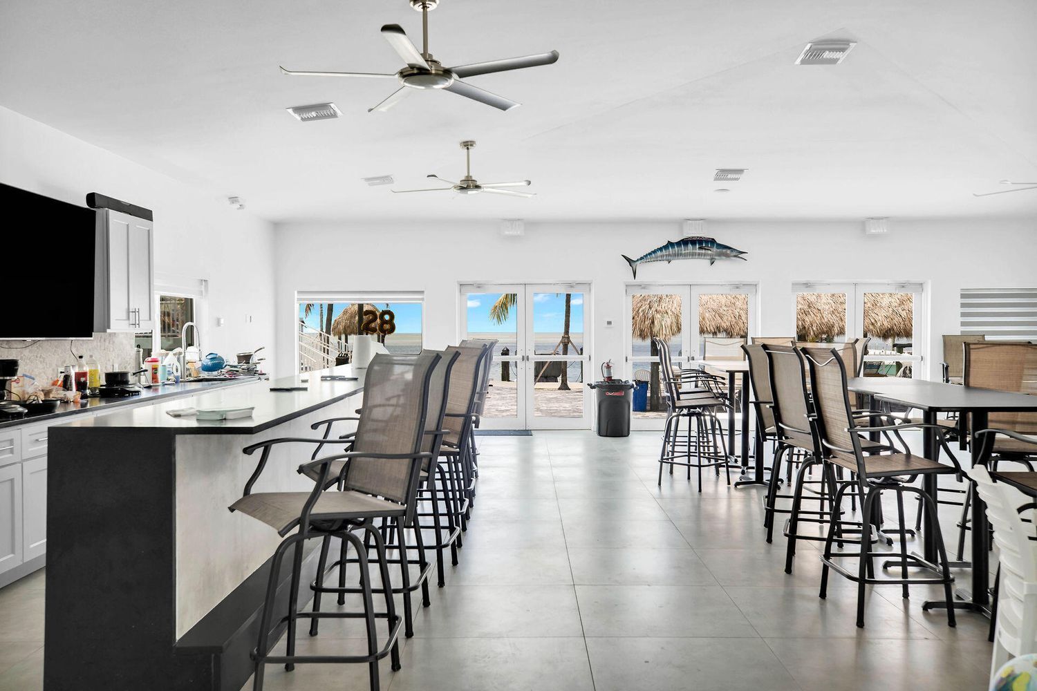A spacious kitchen with a large island, multiple ceiling fans, and a view of the beach through large doors.