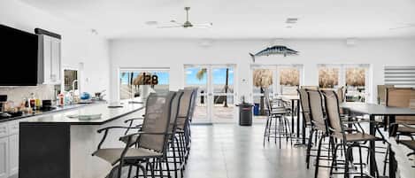 A spacious kitchen with a large island, multiple ceiling fans, and a view of the beach through large doors.