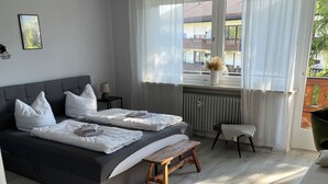 Ein modernes Schlafzimmer mit zwei Betten, einer Bank, einem Sessel und Blick ins Freie.