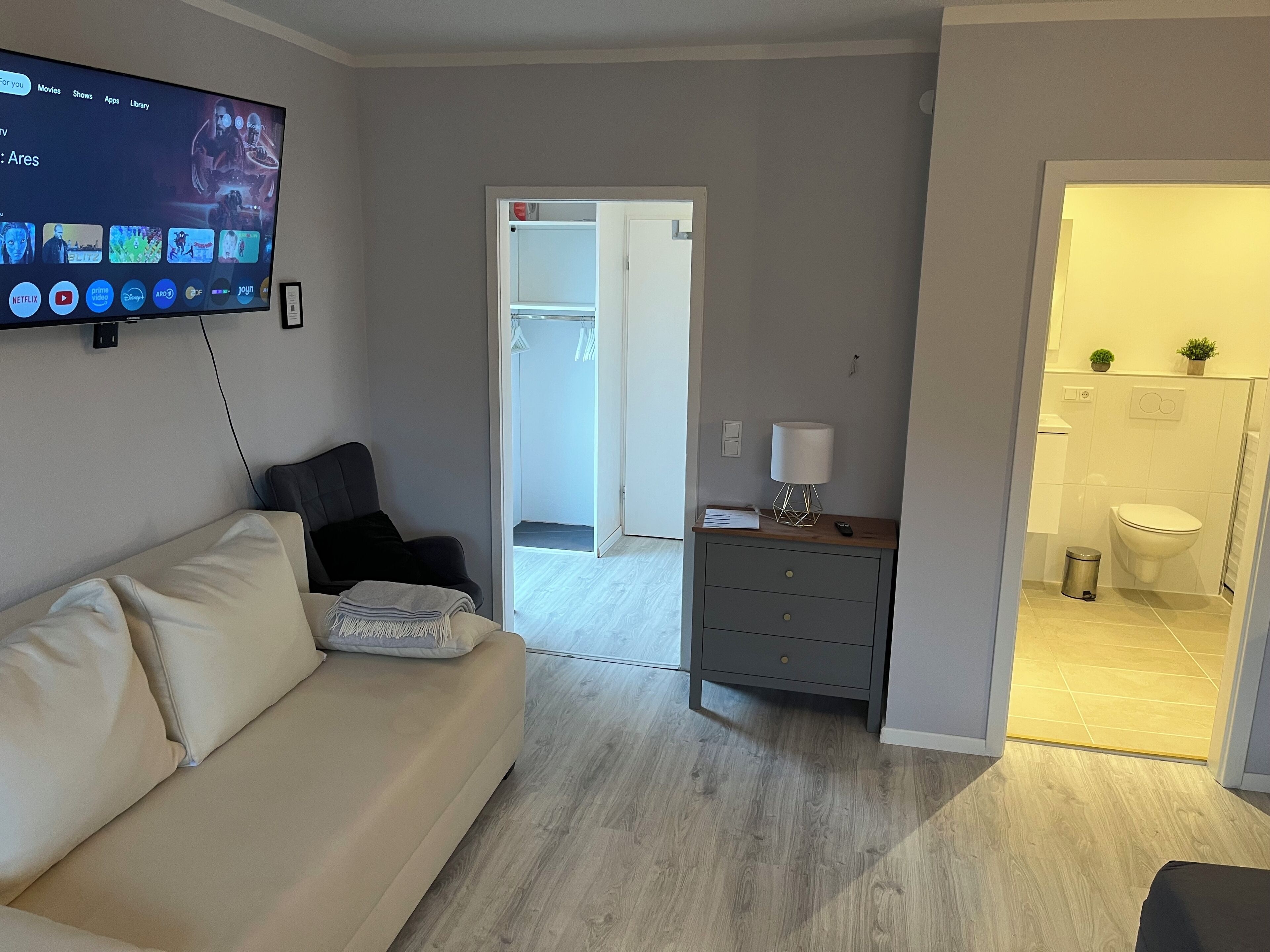 Una sala de estar moderna con un televisor de pantalla plana montado en la pared, un sofá color beige y una mesita de madera con una lámpara.