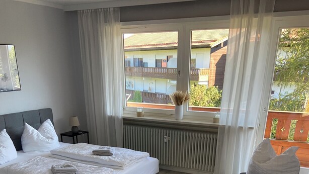 Ein modernes Hotelzimmer mit zwei Betten, einer hölzernen Bank, einem kleinen Tisch und einem Fenster mit Blick nach draußen.