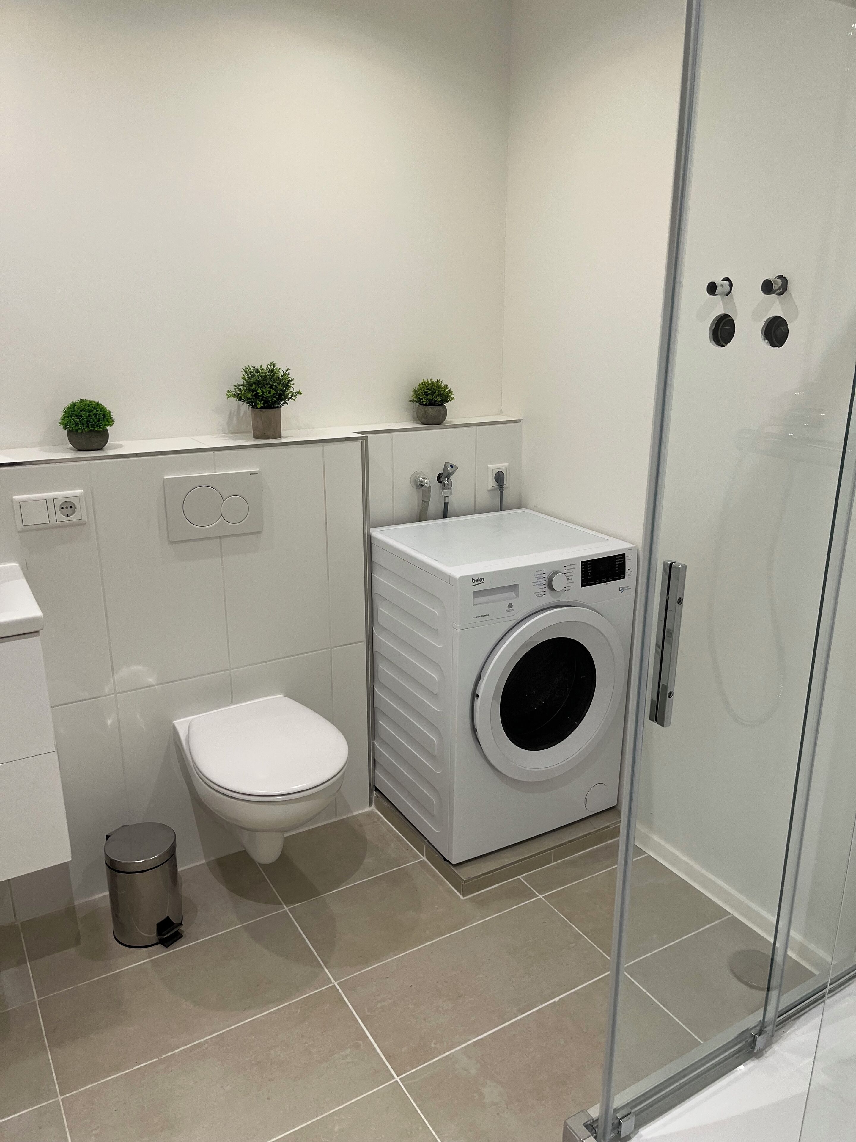 A modern bathroom with a toilet, washing machine, and glass shower enclosure.