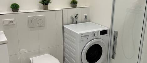 A modern bathroom with a toilet, washing machine, and glass shower enclosure.