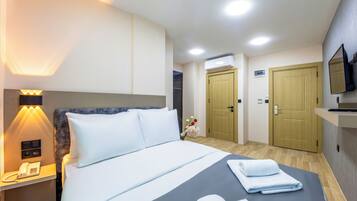Habitación de hotel con cama, lámpara de noche, teléfono y televisor montado en la pared.