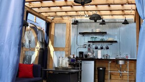 A covered outdoor kitchen area with a dining set and a small refrigerator. - Hocking Hills Airstream & Outdoor Living (McArthur)